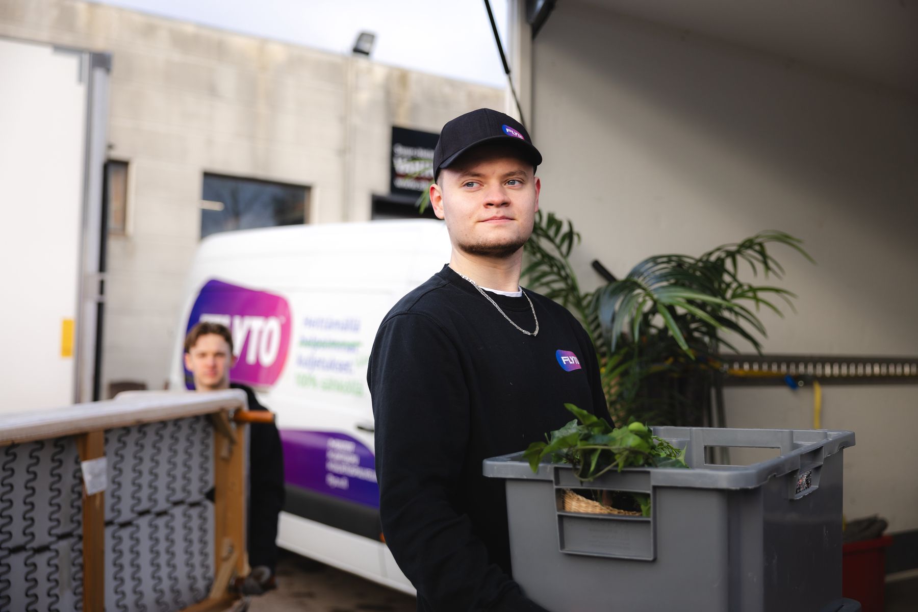 Kaksi Flyton muuttajaa kantamassa muuttolaatikoita muuttoauton edessä